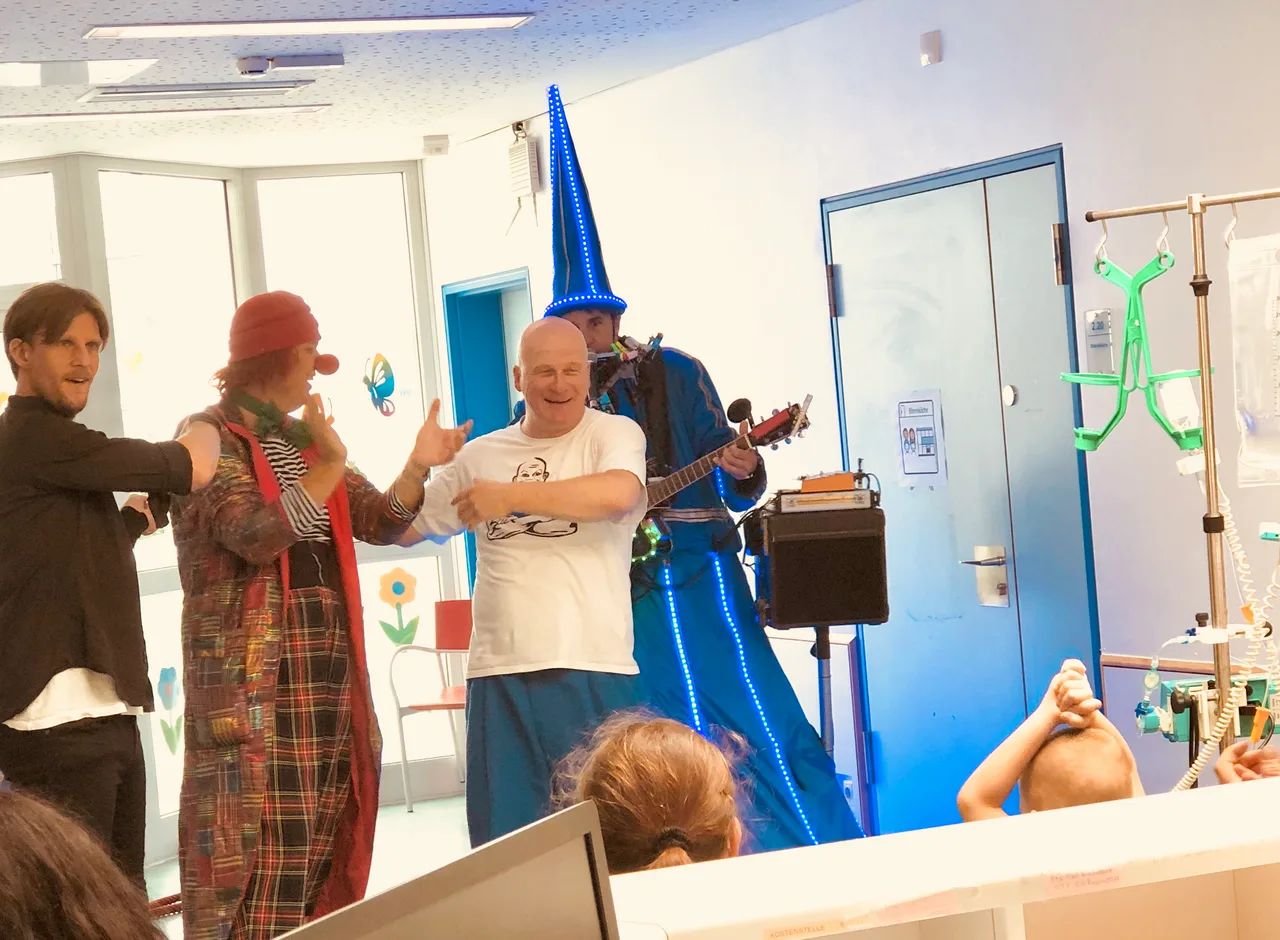 Künstler treten auf einer Kinderkrebsstation auf, Kinder schauen von ihren Betten aus zu.